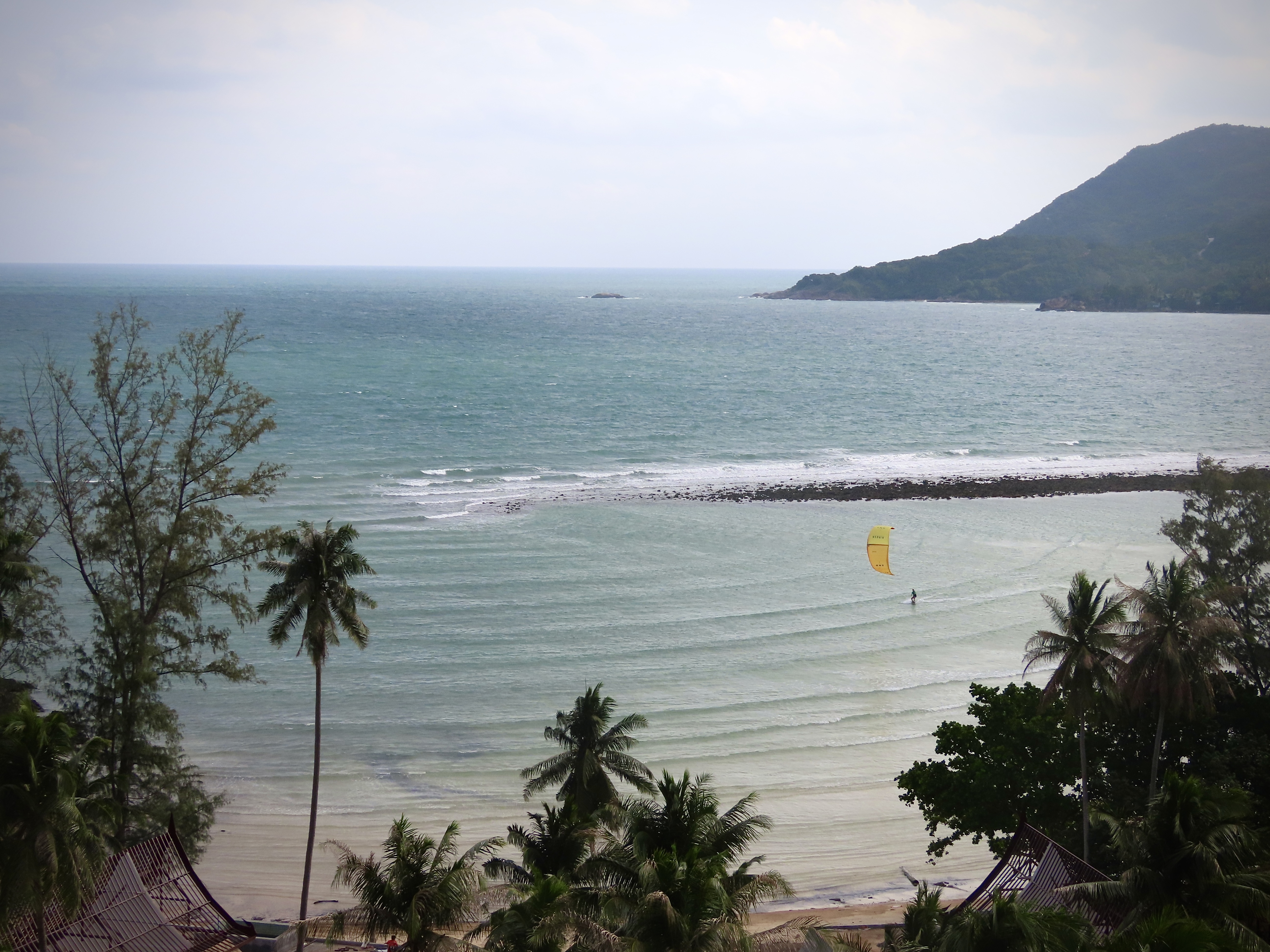 Aerial view of Chaloklum Bay showing the protective reef and flat water lagoon with a lone kitesurfer riding
