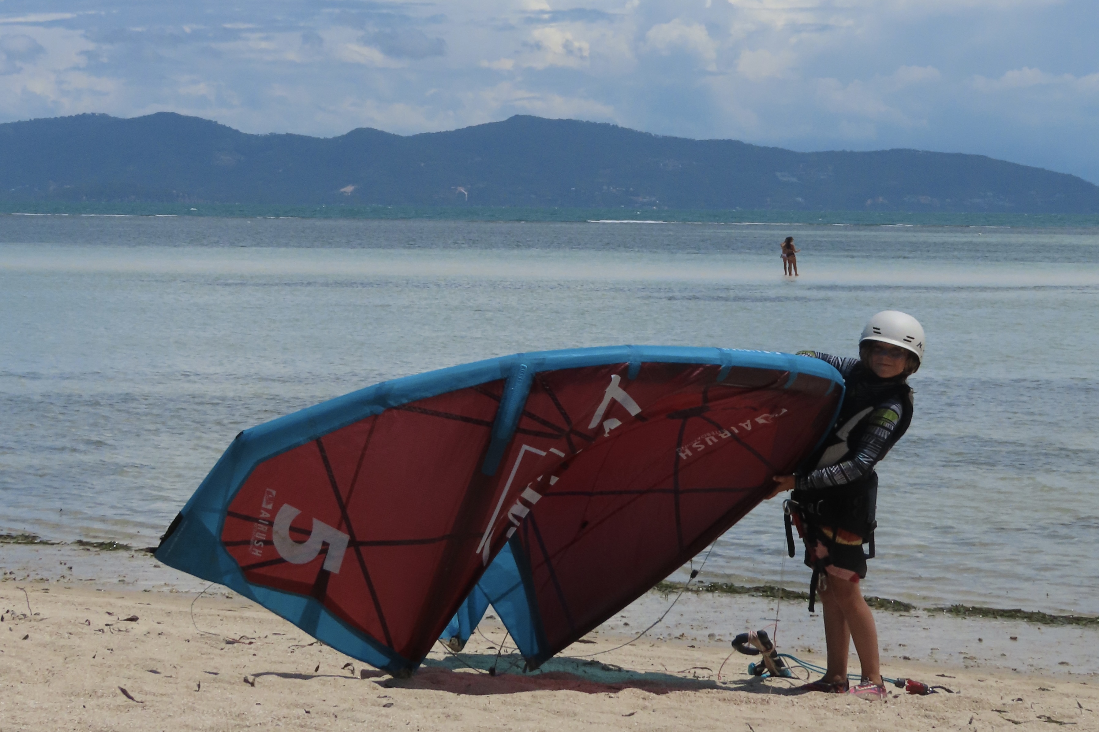 Little girl holding a 5-meter kitesurfing kite on the sandy beach of Koh Phangan, Thailand.