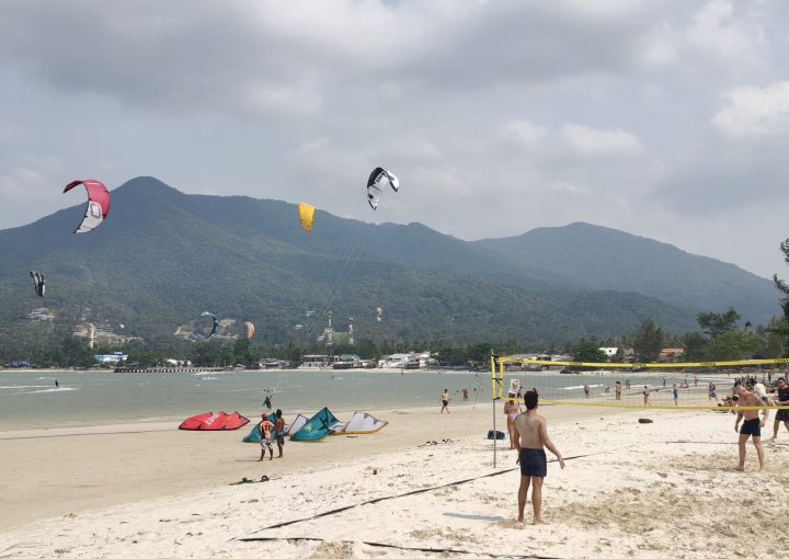 Kitesurfers riding at Chaloklum Malibu Beach with people watching and a strong local kite community vibe