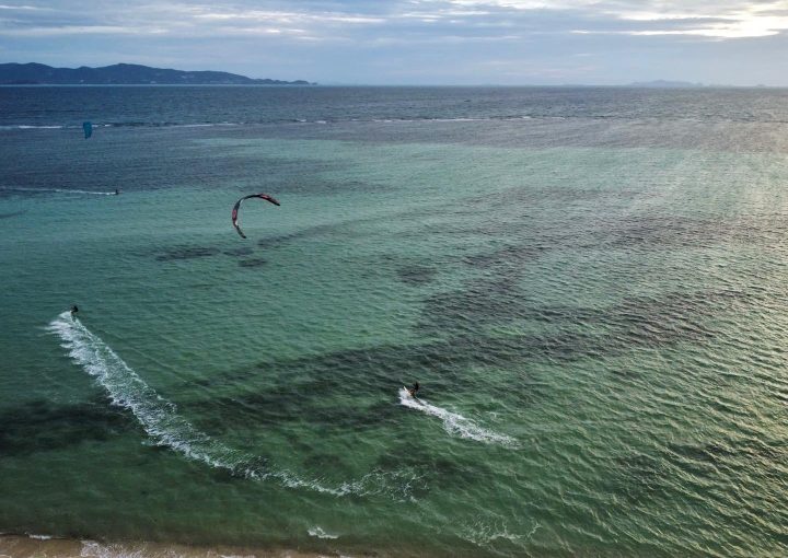 Aerial drone view of multiple kitesurfers riding in Thong Sala Lagoon, Koh Phangan, Thailand, showcasing turquoise waters and tropical winds.