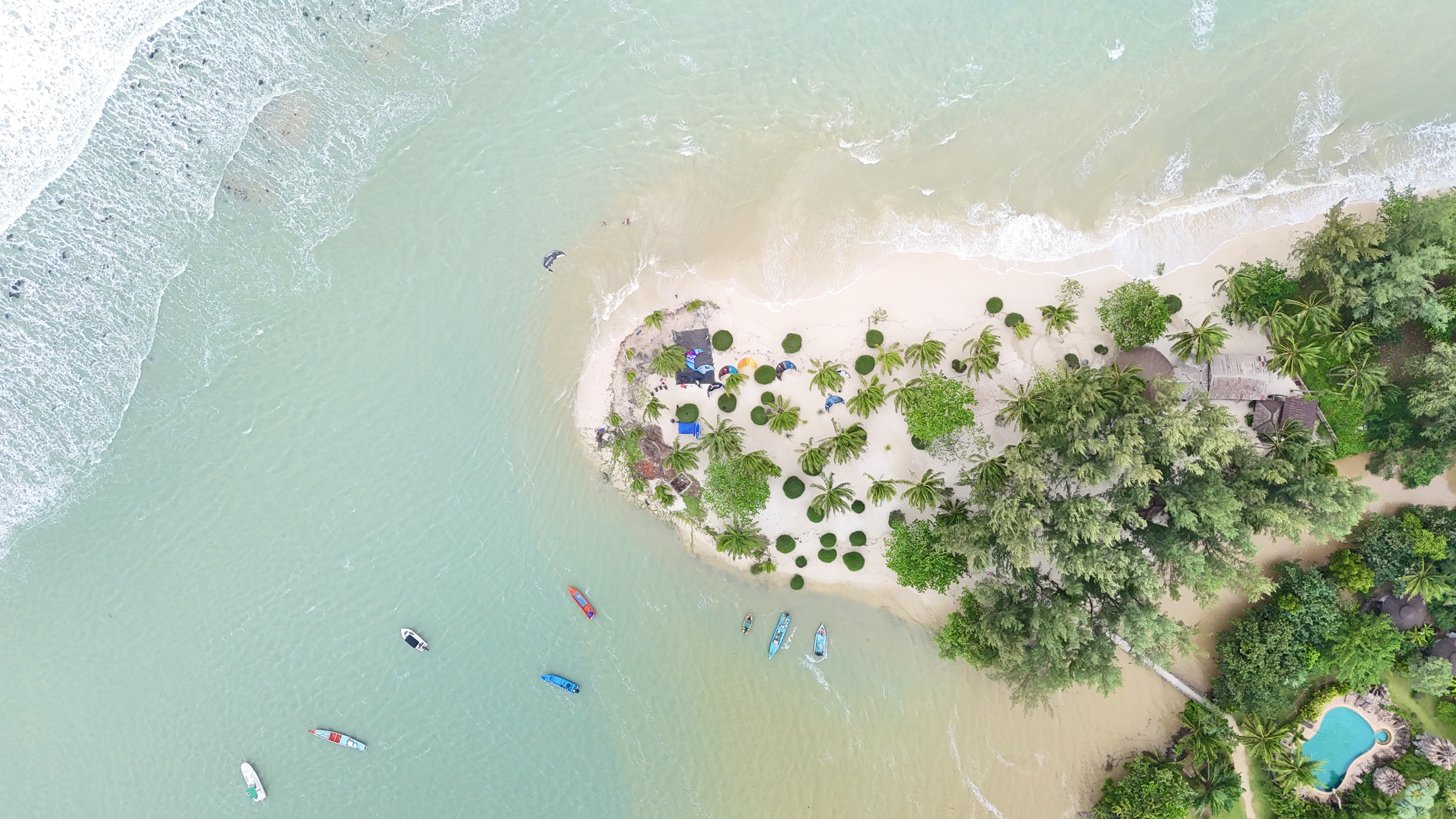 Aerial view of Malibu Beach peninsula in Chaloklum, Koh Phangan with kitesurfing station, palm trees, lagoon and Malibu Resort swimming pool.