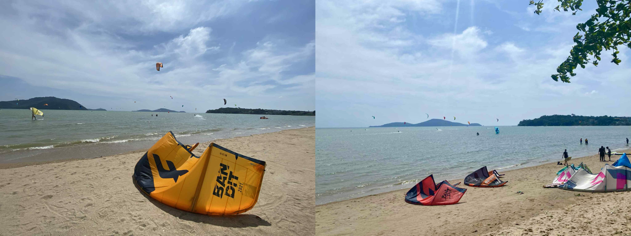 Kites parked on the beach during a windy day at Chalong Bay Thailand with kitesurfers riding in the background.