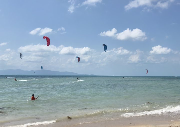 Many kitesurfers riding and launching kites on a very windy day at Baan Tai Beach Siam Pro Kite Koh Phangan Thailand with multiple colorful kites filling the sky and active riders on the water.