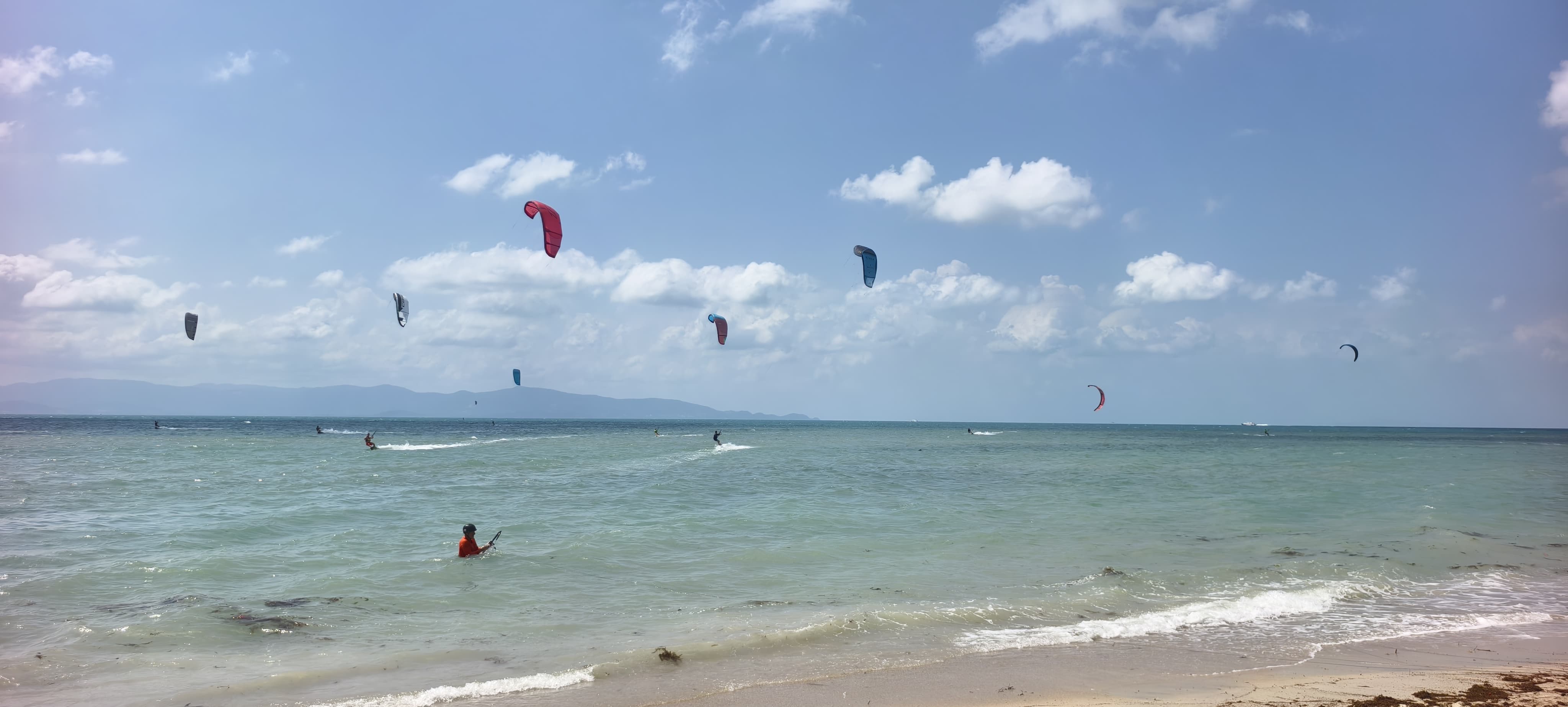 Many kitesurfers riding and launching kites on a very windy day at Baan Tai Beach Siam Pro Kite Koh Phangan Thailand with multiple colorful kites filling the sky and active riders on the water.