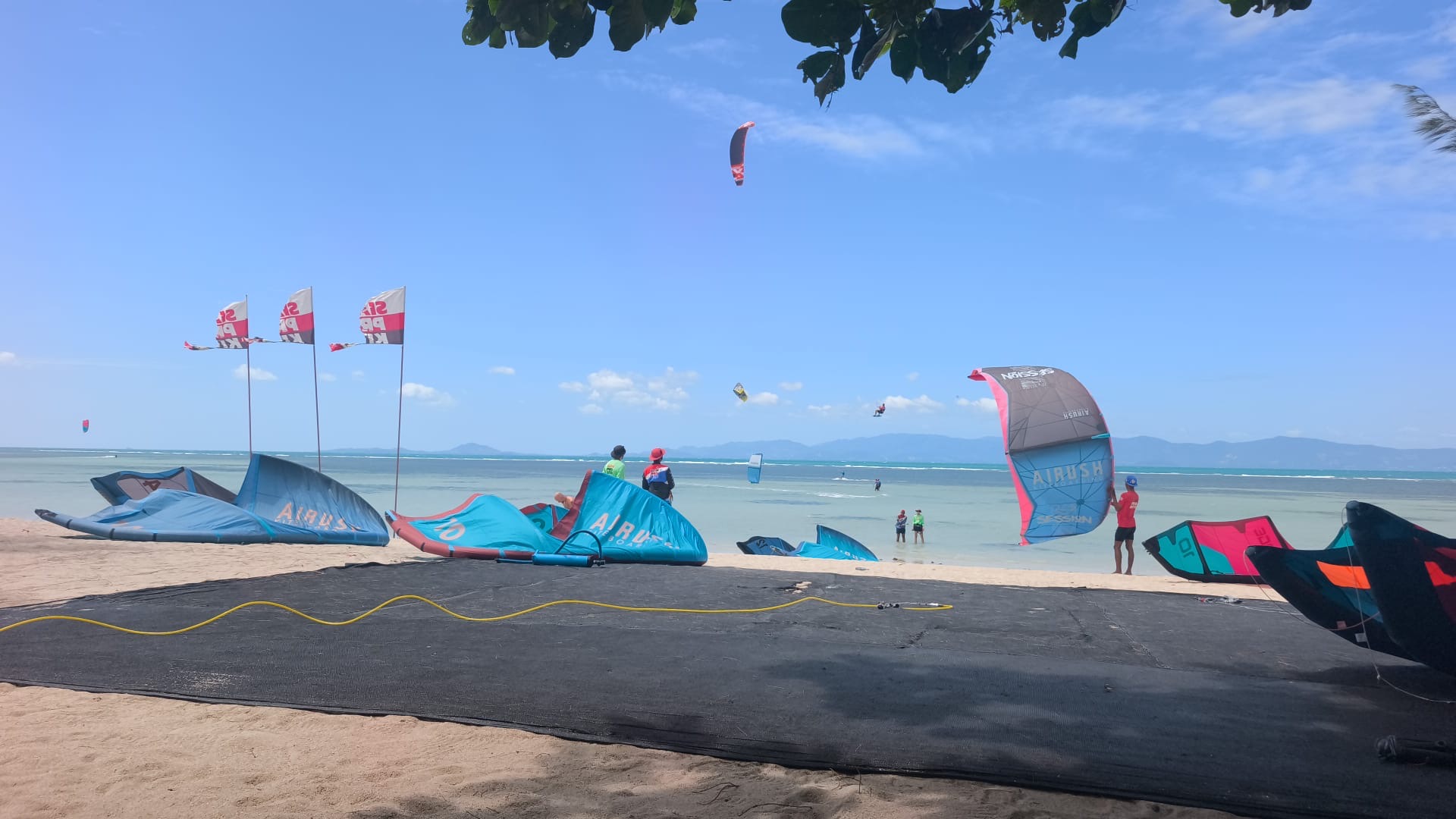 Kitesurfers riding on flat water with large kites at a beginner-friendly beach in Baan Tai, Koh Phangan, Thailand.
